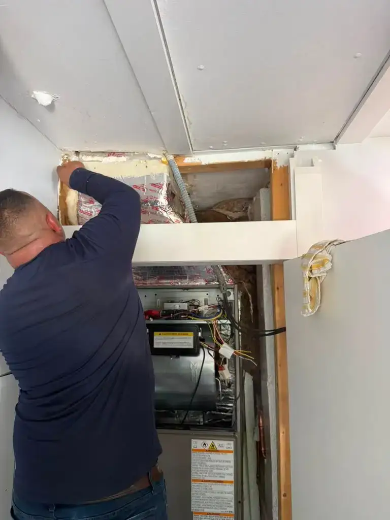 Liberty Air and Electric technician working on an air handler in a Florida utility closet with the ceiling opened up to reach the plenum and duct connections.