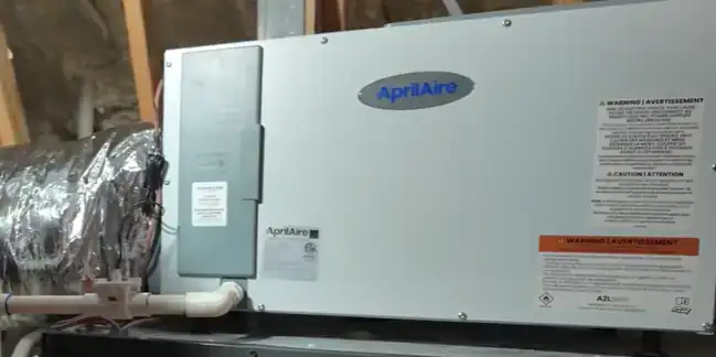 AprilAire whole-house dehumidifier installed in a Florida attic above the air handler, with insulated flex duct connected and a PVC condensate drain run off the cabinet.