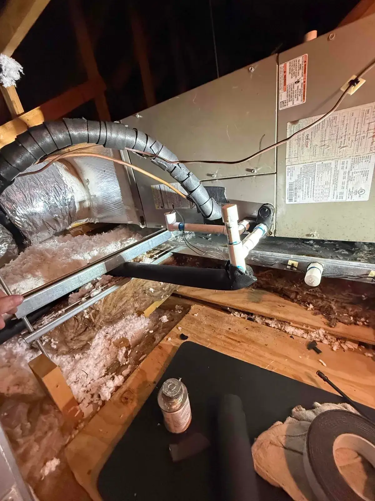 Attic air handler with insulated line set, PVC condensate drain and cleanout tee, and blown insulation, during a Liberty Air and Electric visit in Florida.