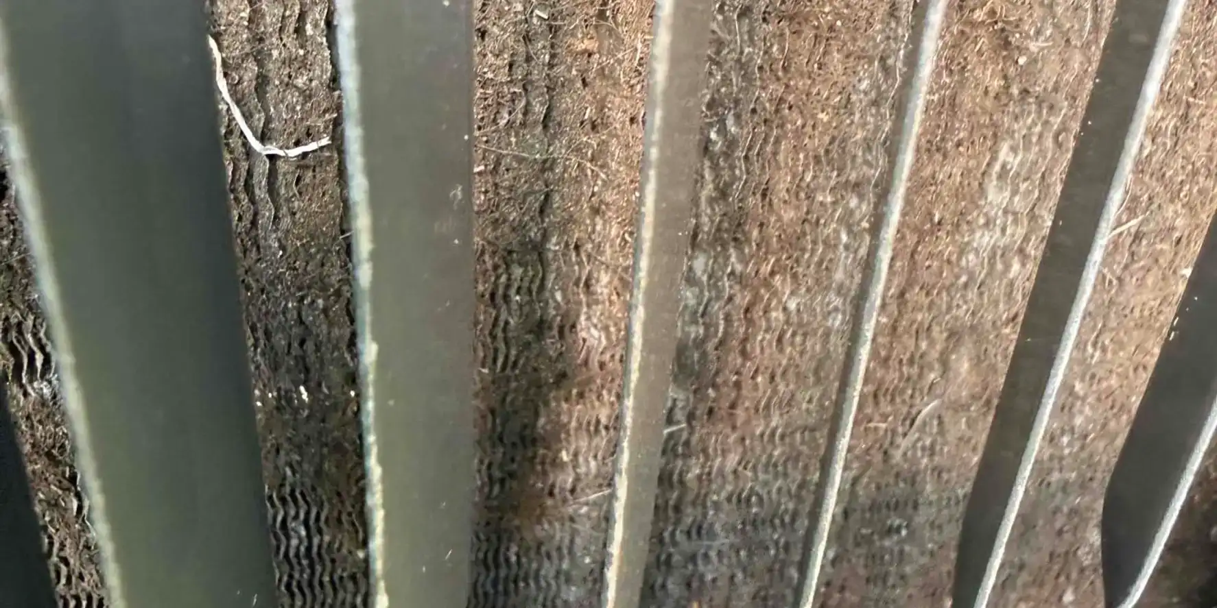 Condenser coil fins packed solid with dirt and grass debris, seen through the fan grille of a Florida AC unit.