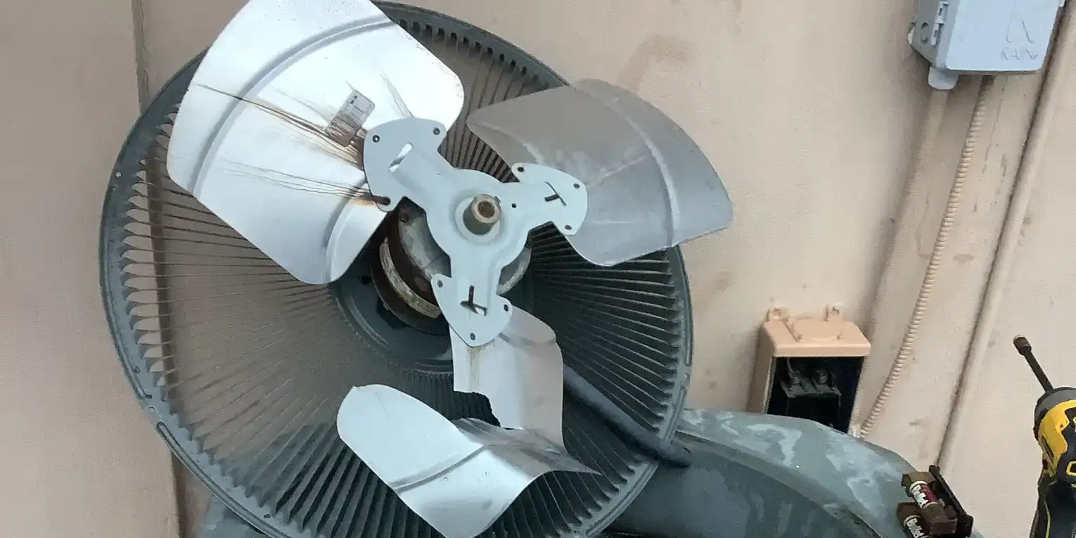 Condenser fan grille lifted off an outdoor unit during a Liberty Air and Electric fan motor replacement, blade and motor shaft exposed.