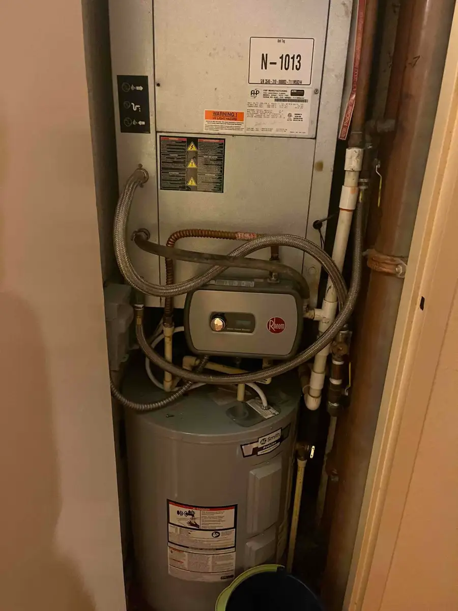 Florida condo mechanical closet with a vertical stack water-source heat pump above a Rheem tankless booster and an A.O. Smith tanked water heater, braided hoses and copper risers filling the remaining space.