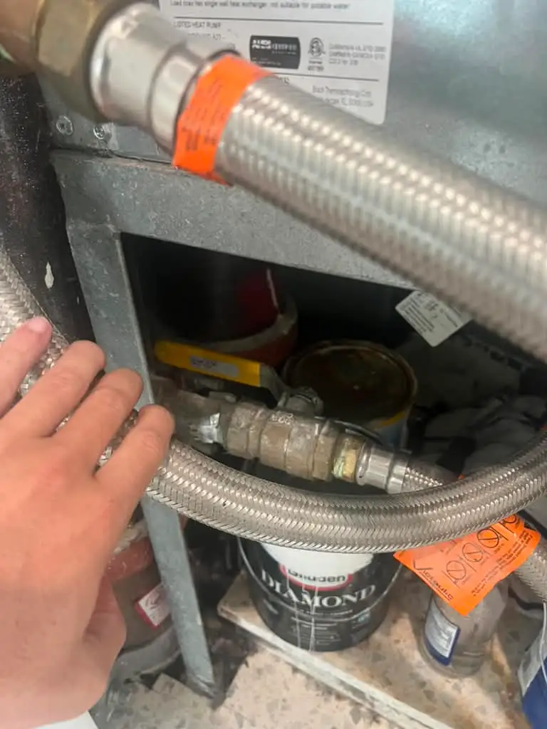Brass ball valve on the condenser water riser inside a Florida condo vertical stack heat pump cabinet, with the braided stainless supply hose running across it.