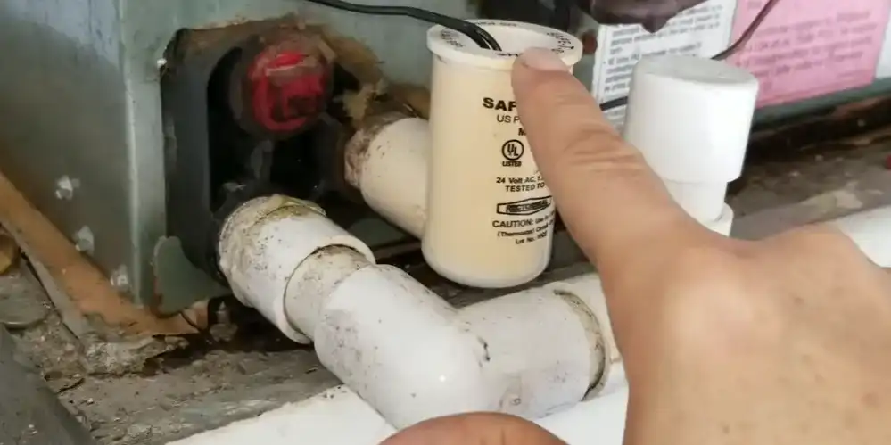 Technician pointing at a Safe-T-Switch float switch on the condensate drain line beside a Florida air handler.
