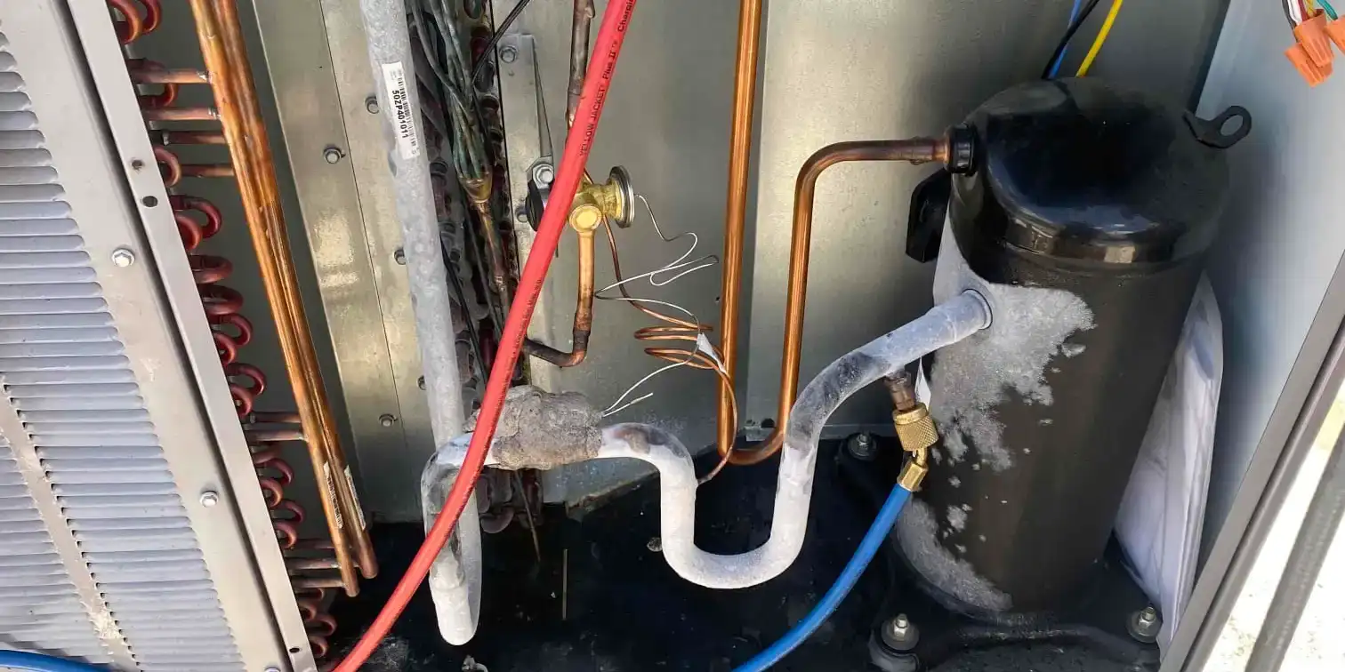 Frost covering the suction line and accumulator inside an open outdoor unit, with refrigerant gauge hoses connected to the service ports.