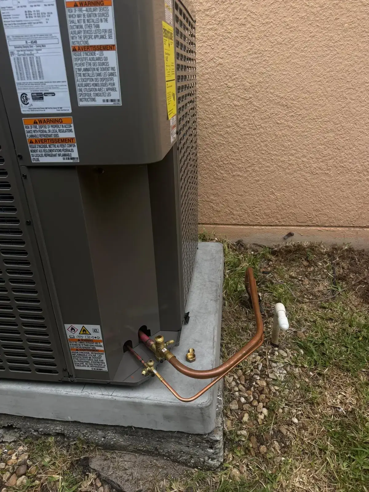 New AC condenser set on a fresh concrete slab with a brazed copper line set and service valves at a Florida home, R-454B refrigerant label visible on the cabinet.