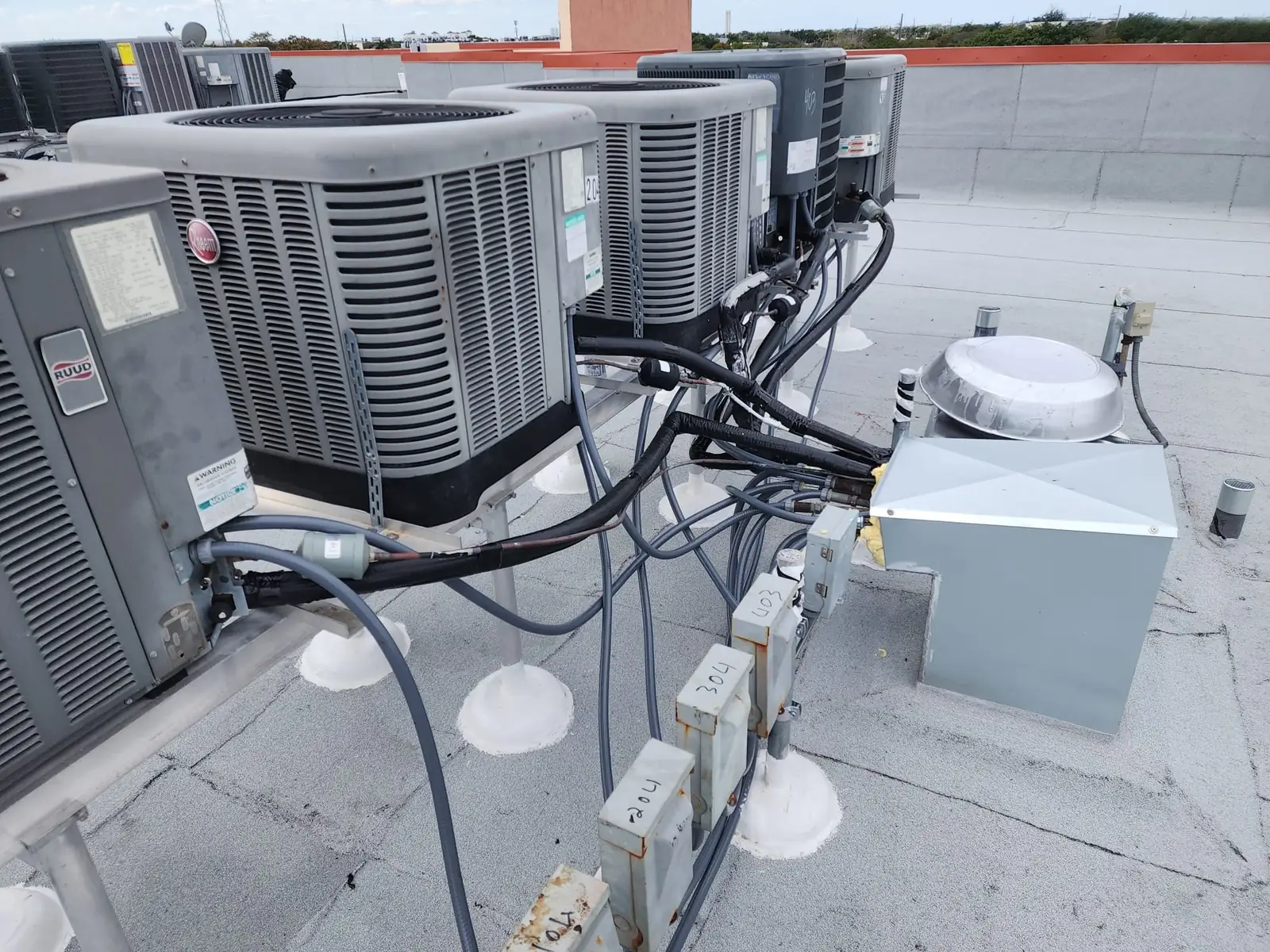 Liberty Air and Electric multi-family rooftop AC reinstallation at Plantation Forest, showing condenser stands, electrical disconnects, and refrigerant line routing.