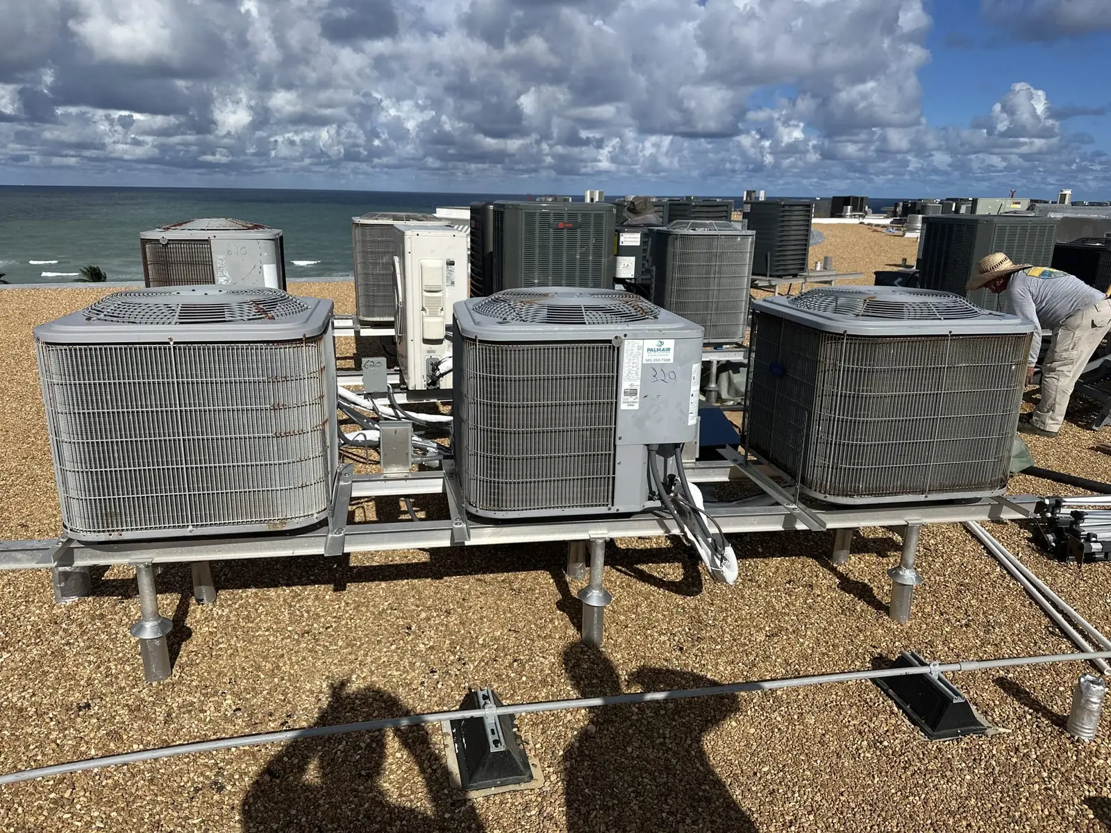 Liberty Air and Electric rooftop AC reinstallation at Sun & Surf, an oceanfront West Palm Beach property, with condensers on HVHZ-rated stands and the Atlantic in the background.