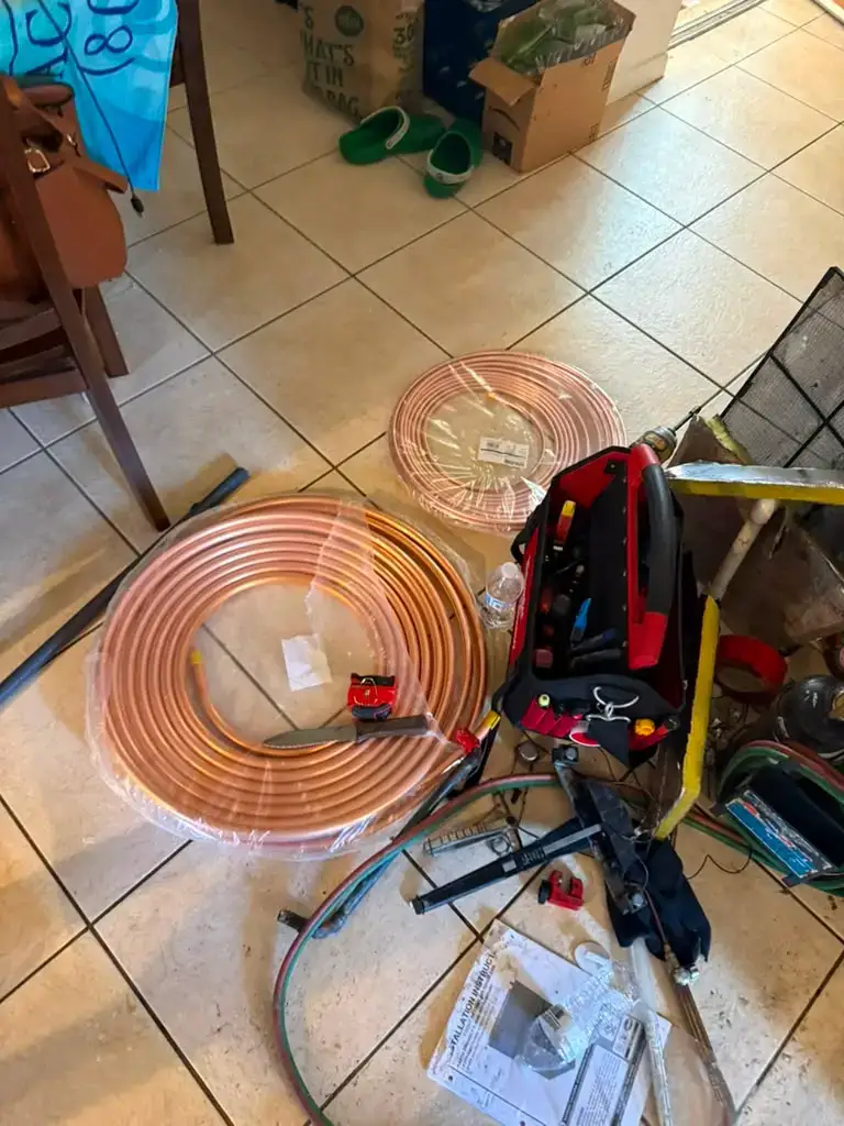 Coils of new copper refrigerant line set staged on the floor next to brazing torch and hand tools before a Florida AC installation.