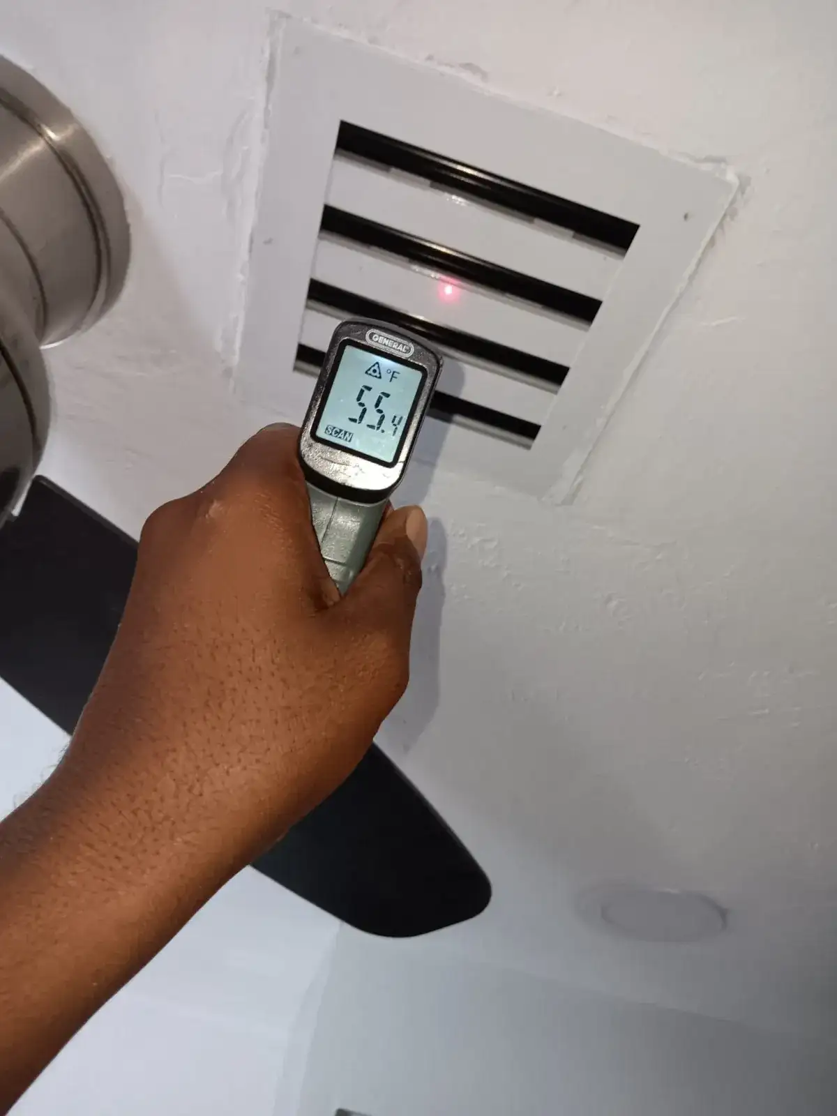 Liberty Air and Electric tech holding an infrared thermometer reading 55.4 degrees at a ceiling supply register during a Florida maintenance visit.