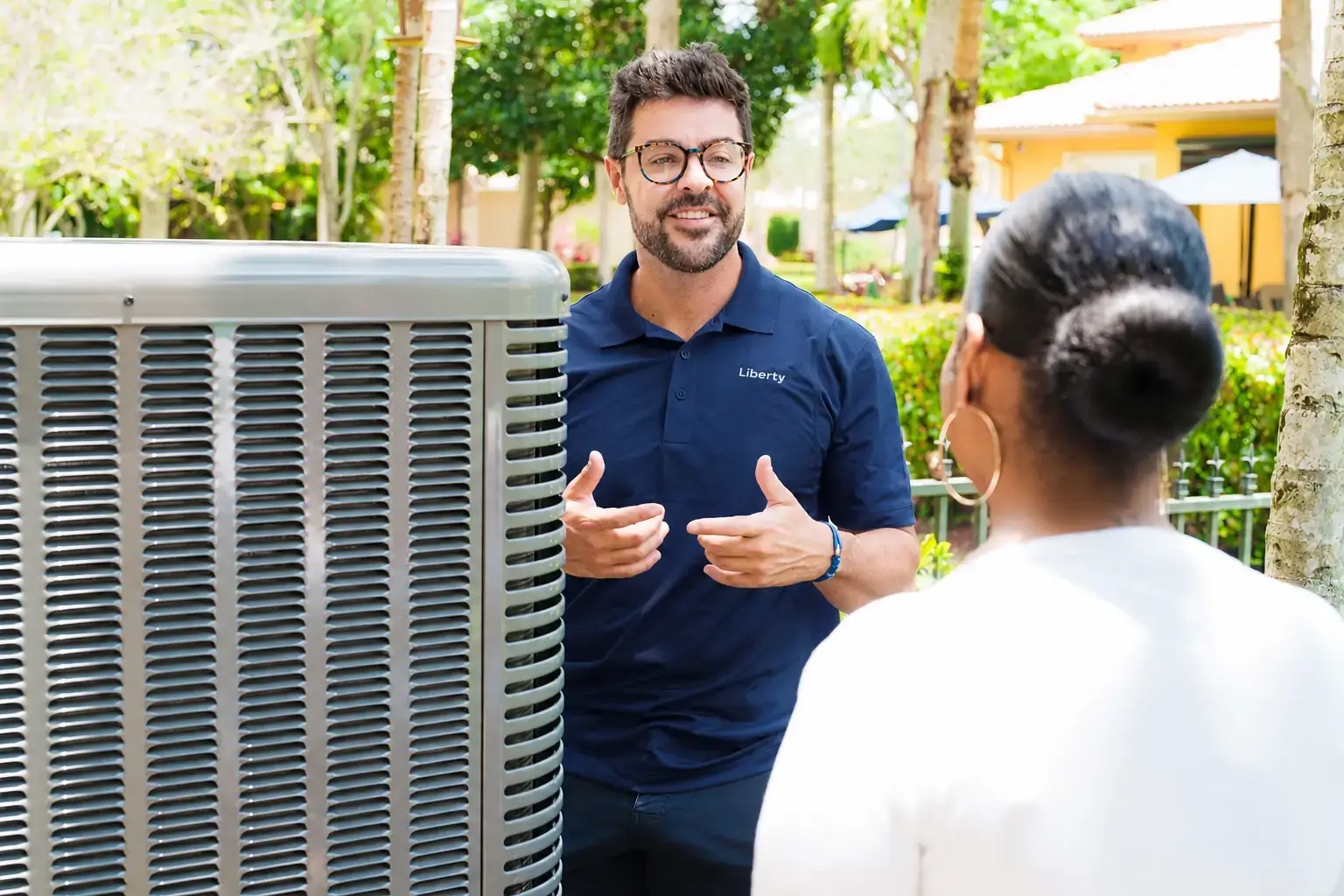 Liberty Air and Electric tech walking a homeowner through an AC repair-vs-replace analysis next to an outdoor condenser at a Florida home.