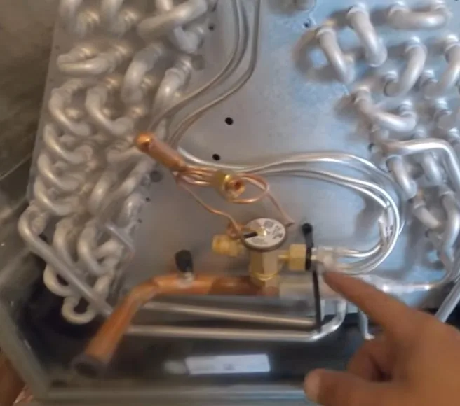 Liberty Air and Electric technician pointing at the brass TXV and its copper lines on a Trane all-aluminum indoor coil.