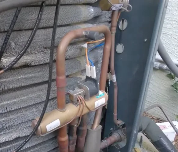 Brass reversing valve and copper refrigerant lines on a Trane heat pump outdoor unit, with the fine aluminum Spine Fin coil filling the background.